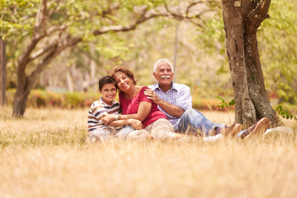 Großelternpaar umarmt kleinen Jungen im Gras - Foto, Bild