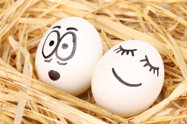 Білі яйця зі смішними обличчями в соломі
 - Фото, зображення