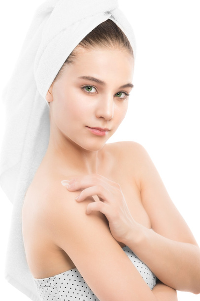 Donna con viso pulito e asciugamano sulla testa applicando crema idratante sulle spalle. Isolato
. - Foto, immagini