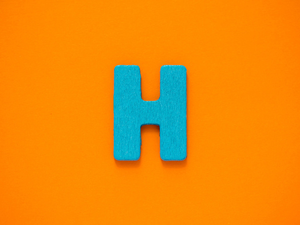 Capital letter H. Blue letter H from wood on orange background. - Fotó, kép