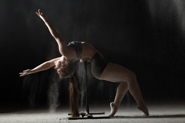 Woman doing gymnastic element on stand while sprinkled flour - Foto, Imagen
