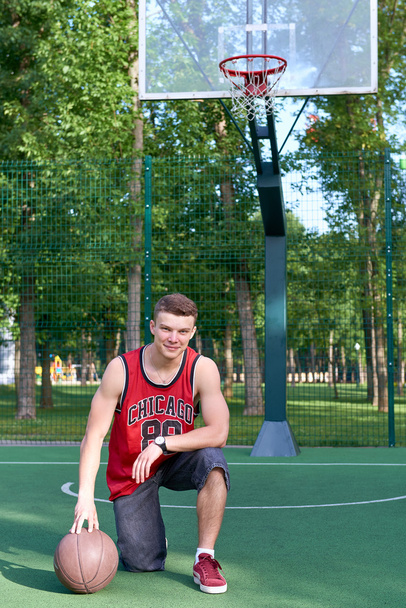 B-boy zittend op basketbalveld met bal - Foto, afbeelding