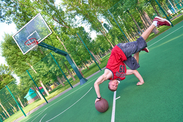 B-boy haciendo truco de acrobacias en el campo de baloncesto con pelota
 - Foto, Imagen