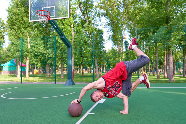 B-boy haciendo truco de acrobacias en el campo de baloncesto con pelota
 - Foto, Imagen