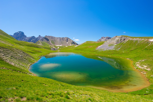 High altitude blue lake in idyllic uncontaminated environment once covered by glaciers. Summer adventures and exploration on the Italian French Alps. Expansive view from above, clear blue sky. - Photo, Image