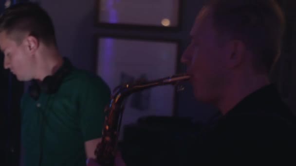 Dj spinning at turntable on party in nightclub. Man play saxophone. Duet. - Video, Çekim