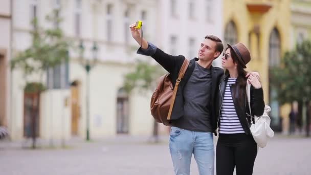 Romantic couple walking together and taking selfie in Europe. Happy lovers enjoying cityscape with famous landmarks. Stylish urban young man and woman with backpacks on travel. - Felvétel, videó