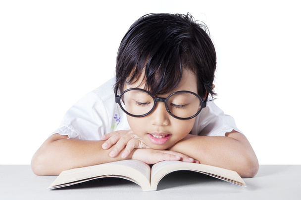 Досить маленька дівчинка в окулярах читає книгу
 - Фото, зображення