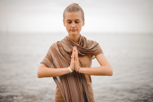 Frau in dankbarer Namaste-Yoga-Pose am Strand neben dem Meer bei bewölktem Wetter. Zen, Meditation, Frieden. - Foto, Bild