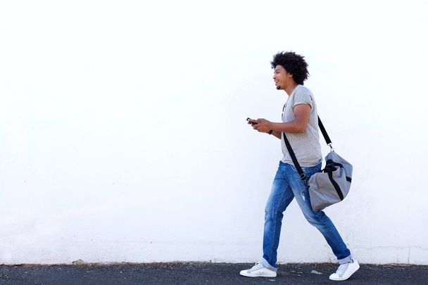 Jonge man lopen met de tas en mobiele telefoon - Foto, afbeelding