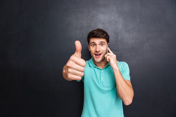 Surprised man talking on mobile phone and showing thumbs up - Photo, Image