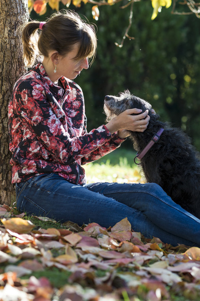 Woman sitting under a tree fondling her dog - Photo, Image