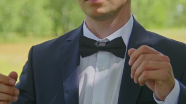 De bruidegom in een wit overhemd zet op een strik aan de voorkant, buiten, close-up. - Video