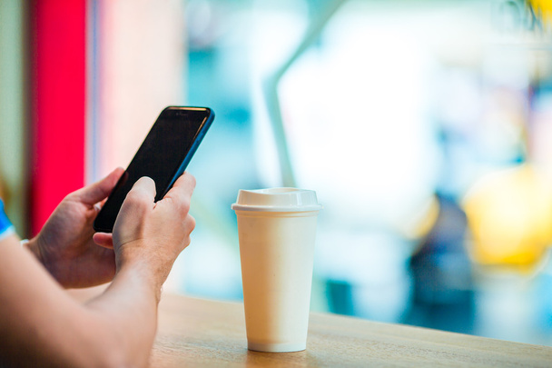Detailní záběr mužských rukou držících mobil a sklenici kávy v kavárně. Muž používající mobilní smartphone. Chlapec se dotýká obrazovky svého chytrého telefonu. Rozmazané pozadí, vodorovné. - Fotografie, Obrázek
