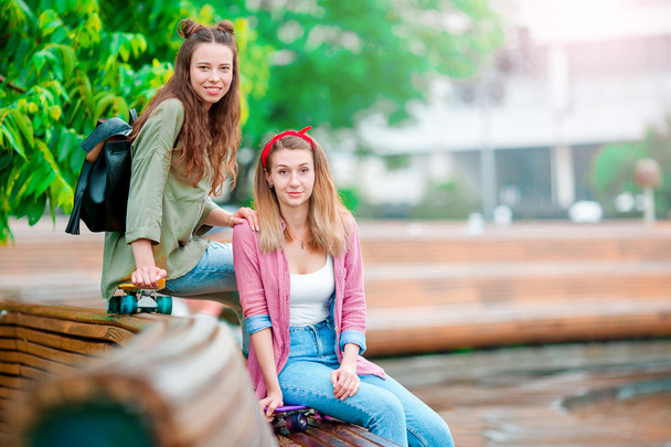 Δύο ευτυχισμένα κορίτσια με σκέιτμπορντ σε εξωτερικούς χώρους. Ενεργές αθλητικές γυναίκες που διασκεδάζουν μαζί σε πάρκο πατινάζ. - Φωτογραφία, εικόνα