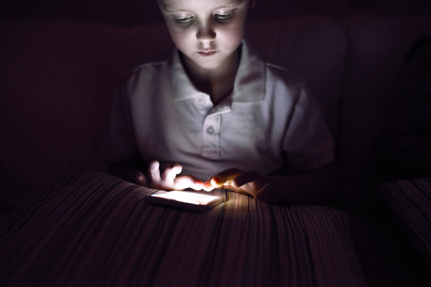kleiner Junge, im Dunkeln sitzend, mit Smartphone spielend - Foto, Bild