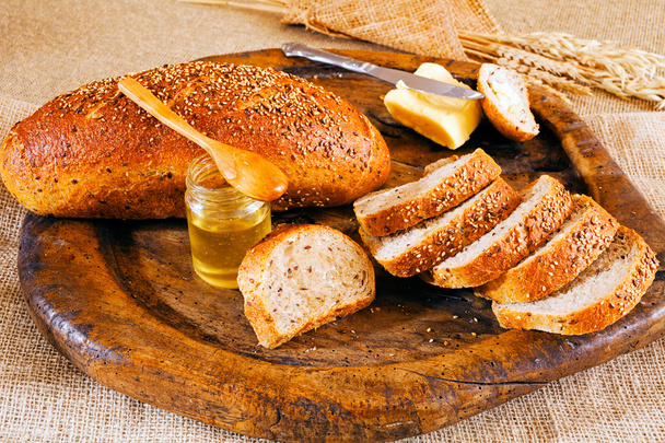 Rebanadas de pan integral sobre tabla de cortar redonda de madera, mantequilla y miel
 - Foto, Imagen