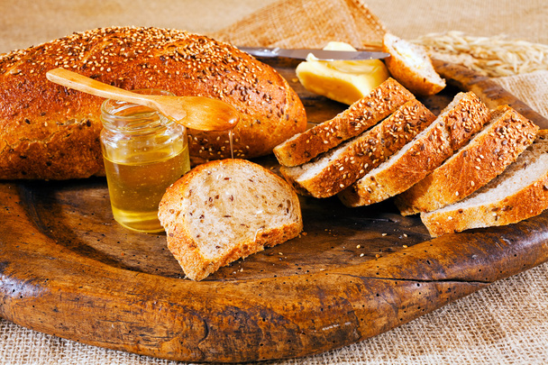 Integraal brood op ronde houten snijplank, boter en pot honing - Foto, afbeelding