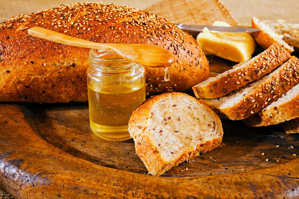 Pan integral sobre tabla de cortar redonda de madera, mantequilla y tarro de miel
 - Foto, Imagen