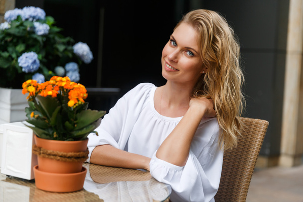 Blonde young woman sitting at the table with flowers - Photo, image