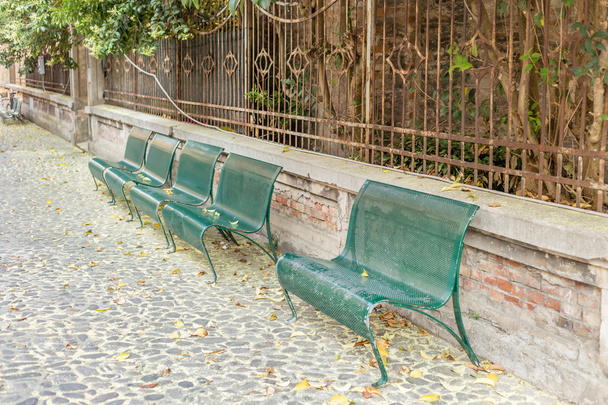 ławki z zielonej żelaza ułożone w brukowanej uliczce z liśćmi i pyłkiem - Zdjęcie, obraz