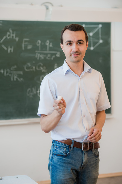 Jóképű fiatal férfi tanuló vagy tanár állandó kellemes szemben egy zöld tábla - Fotó, kép