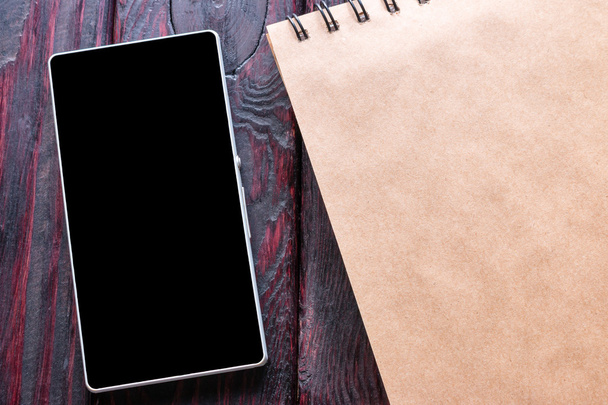 Smartphone lies next to a notebook on a black background - Valokuva, kuva