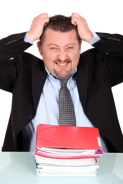 Businessman tearing his hair out over a pile of paperwork - Фото, изображение