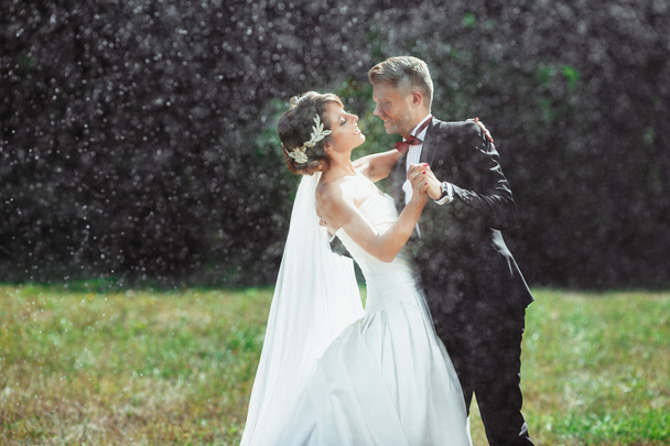 Νύφη και γαμπρός αγκαλιάζοντας και χαμογελαστός υπό βροχή - Φωτογραφία, εικόνα