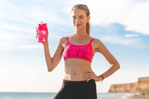 Young woman with pink bottle on the beach - Foto, Imagen