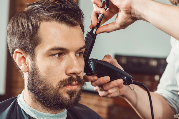 The hands of young barber making haircut attractive man in barbershop - Fotó, kép