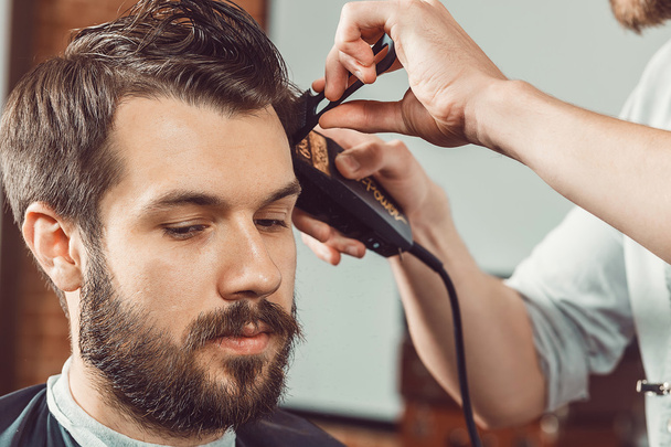 The hands of young barber making haircut  attractive man in barbershop - Fotó, kép