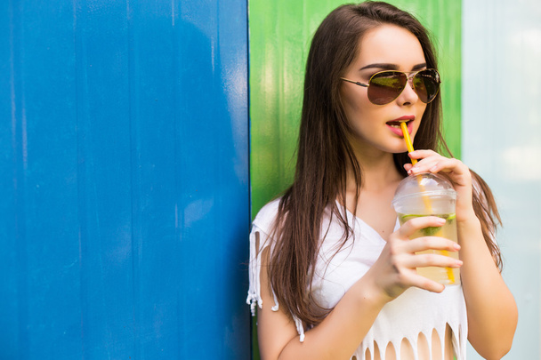žena s nápoj cup v sluneční brýle a čepici přes barvu pozadí - Fotografie, Obrázek