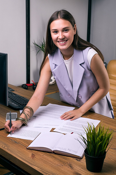 Mujer de negocios sonriente anotando en los documentos en la mesa
 - Foto, Imagen