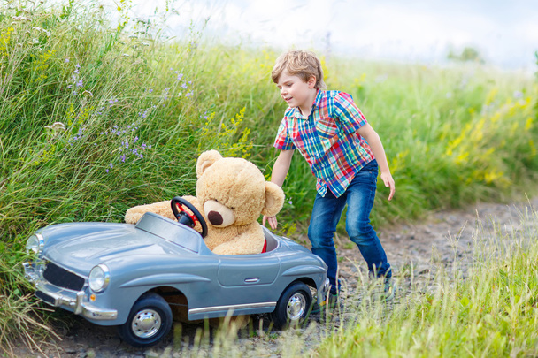 Menino menino dirigindo carro de brinquedo grande com um urso, ao ar livre
. - Foto, Imagem
