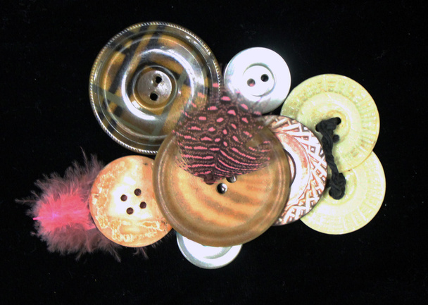Buttons and a pink  feather assortment against a black surface - Photo, Image