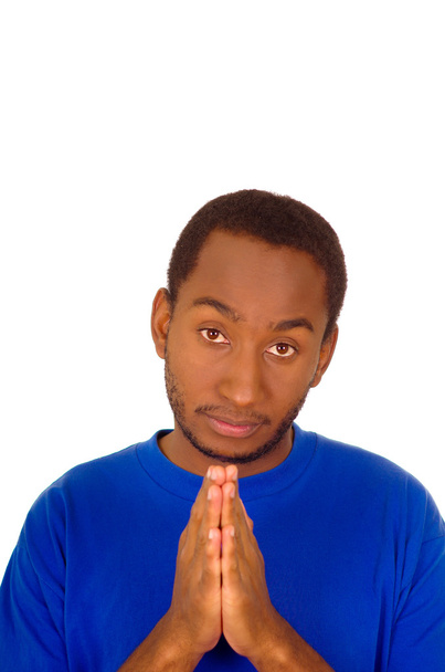 Headshot man wearing strong blue colored t-shirt folding hands in prayer and looking into camera - Foto, imagen