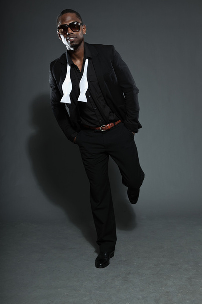 Cool black american man in dark suit. Studio fashion shot isolated on grey background. Wearing dark sunglasses. - Photo, image
