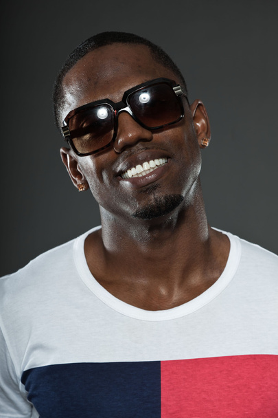 Cool urban stylish black american man. Fashion studio portrait isolated on grey background. Wearing dark sunglasses. Smiling. - Фото, изображение