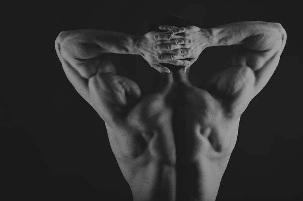Muscular, relief body bodybuilder on a black background. Black a - Zdjęcie, obraz
