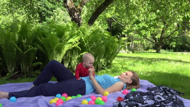 Gelukkig moeder lag op plaid met baby dochter op plaid in zomer park. 4k - Video