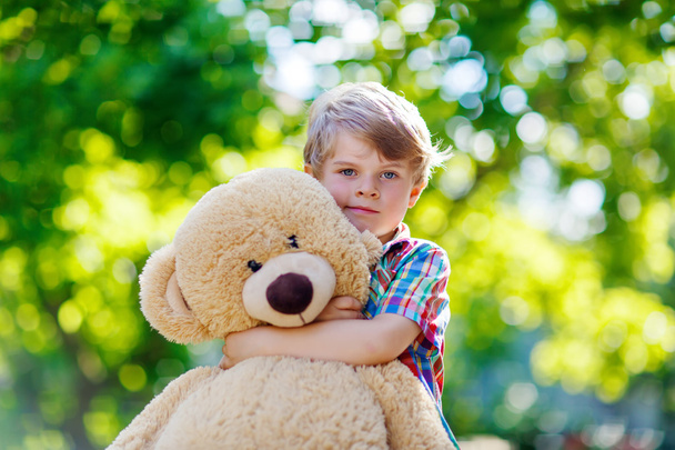 Little kid boy playing with big plush bear, outdoors. - Foto, immagini