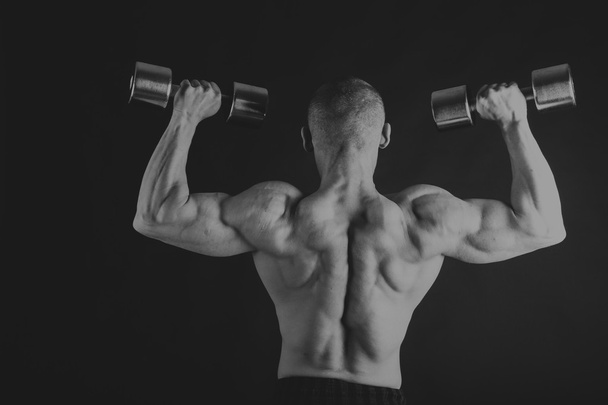 A man with a dumbbell on a black background - Photo, Image