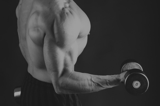A man with a dumbbell on a black background - Photo, Image