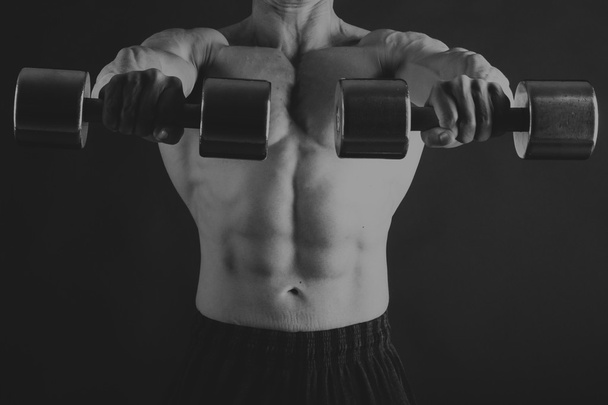 A man with a dumbbell on a black background - Photo, image