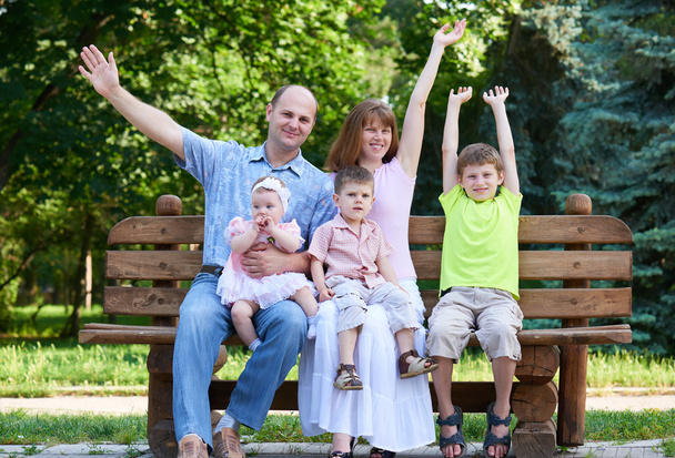 щасливий сімейний портрет на відкритому повітрі, група з п'яти чоловік сидить на дерев'яній лавці в міському парку, літній сезон, дитина і батько
 - Фото, зображення