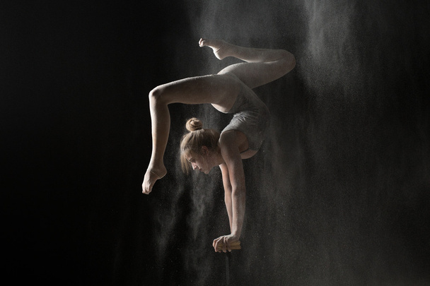 Gymnastic flexible woman handstand on equilibr at sprinkled flour - 写真・画像