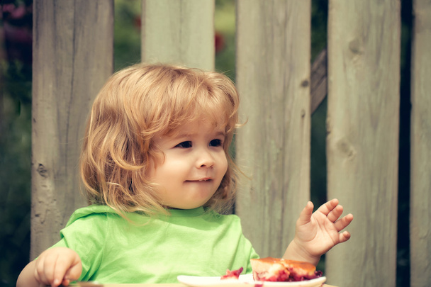 small boy eating pie near wooden fence - Foto, immagini