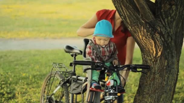Anyám gondoskodik egy gyönyörű kisfiú egy kerékpár ülés a parkban - Felvétel, videó