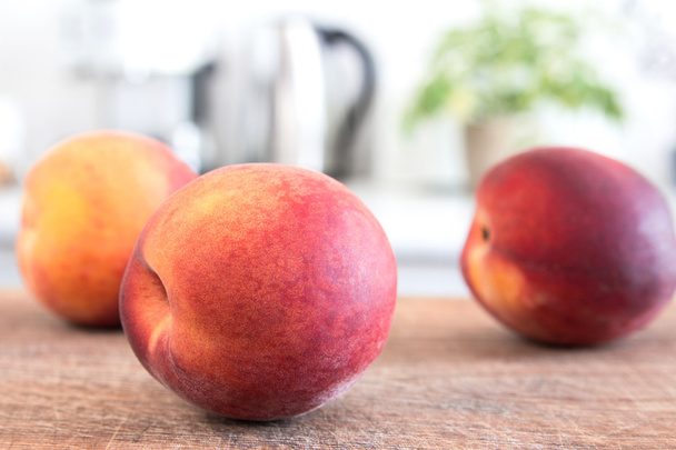 Few peaches on wooden board. White modern kitchen at the background - Photo, Image
